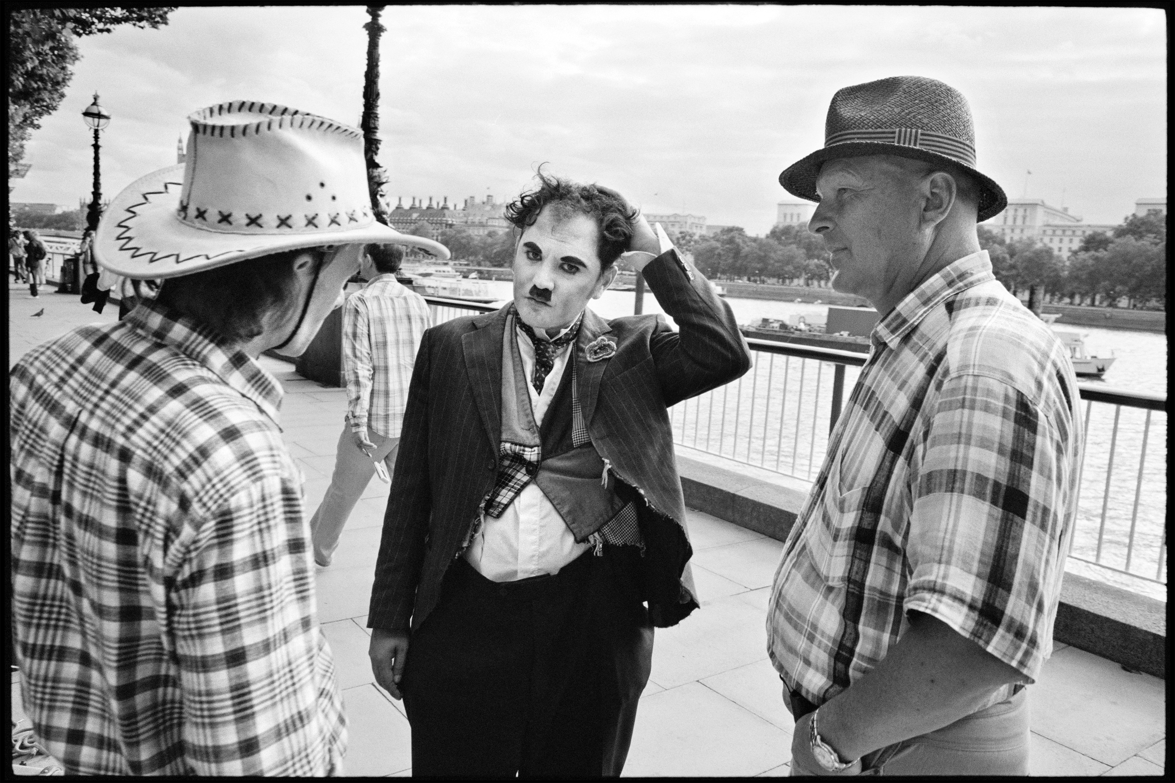 Trois hommes qui discutent, dont l’un a le visage maquillé à la Charlie Chaplin.