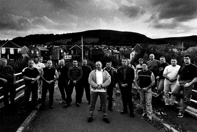 Black and white photo of a group of men posing in front of houses
