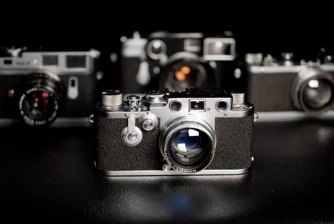 Four Leica Cameras standing on a dark table.