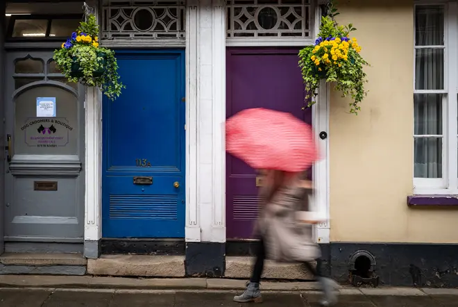 A person is walking past three colorful front doors, holding an umbrella.