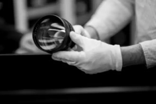 A person is holding a Leica lens while wearing gloves.