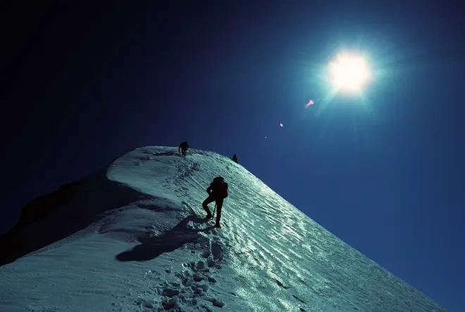 Three persons on the glacier in the dark, illuminated by the moon.