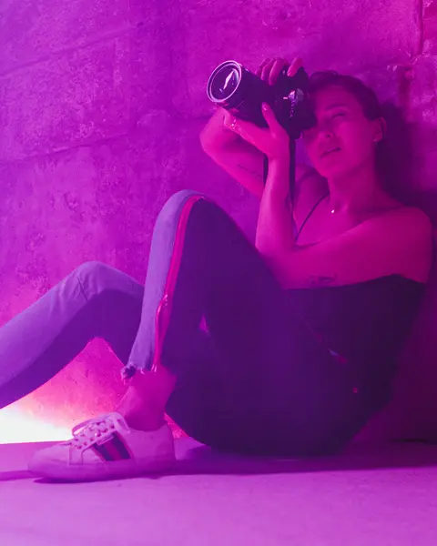 Alex Drewniak sits on the floor, taking pictures in a room lit by pink-purple light.