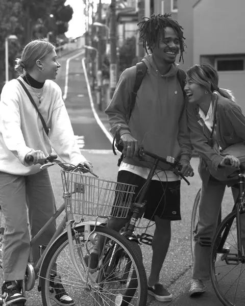 Three young people stand on bicycles in the street and laugh together.