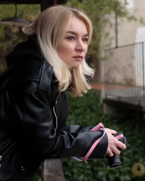 Woman on a balcony holding a camera in her hands.