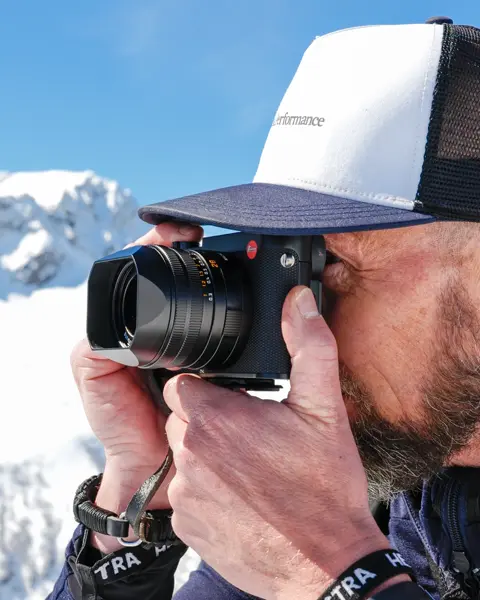 A man takes a photograph in a snowy mountain landscape.