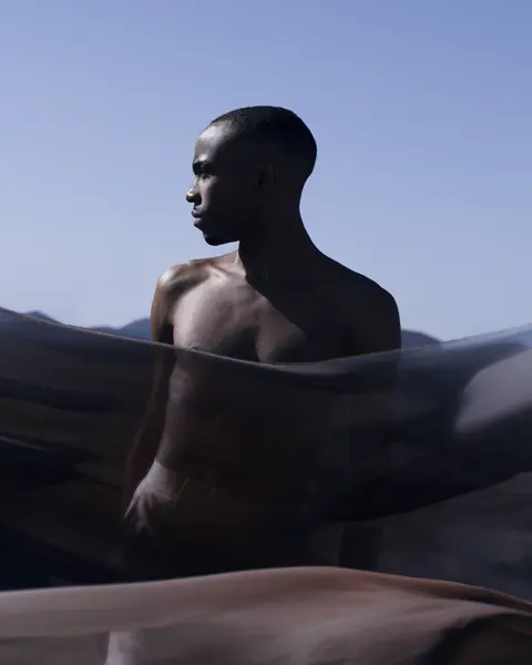 Man behind a transparent cloth looks to the side and light blue sky in the background.
