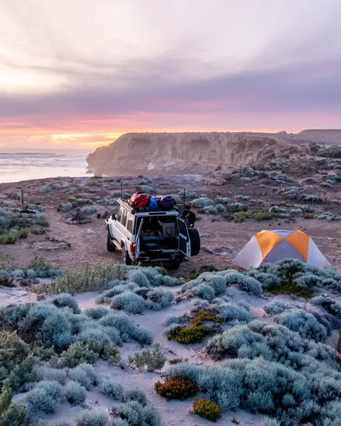 A jeep and two tents on a coast at sunset.
