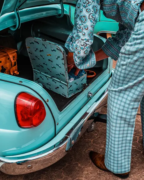 A person packs suitcases into the trunk of a turquoise vintage car.