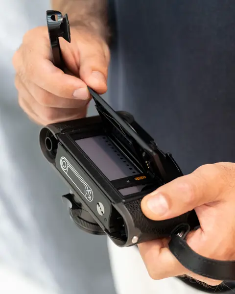Close-up of the hands opening the back of the camera, where the camera roll is placed.