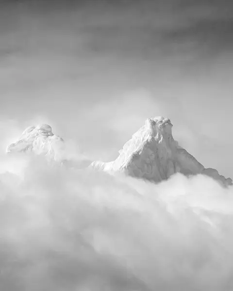 Two snow-covered mountain peaks protrude through a blanket of cloud.