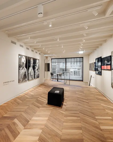 A gallery of Rahi Rezvani's portrait photographs, with the project name Symphony of Faces written on the wall, a light wooden floor and a modern bench.