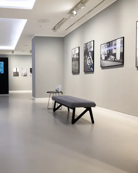 Brightly lit exhibition room with pictures on the wall and benches