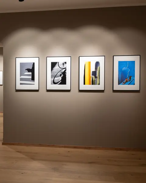 Gallery of black and white and colour photographs on beige walls, discreetly lit and with a light wooden floor.
