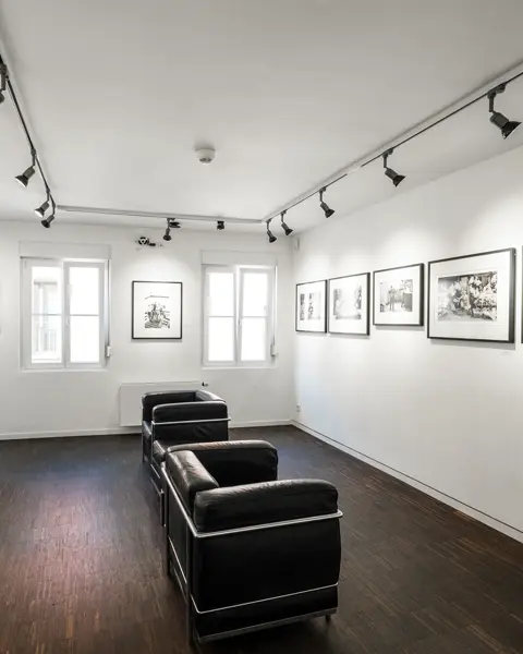 Exhibition room with black and white photographs on the wall and black leather armchairs in the centre of the room.