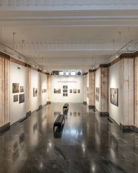 Exhibition room with photographs from different places. At the end of the corridor, on the wall is the writing 'Um clima em mudança', which means 'a changing climate'.