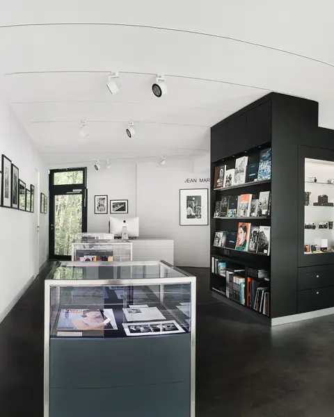 Bright exhibition room with black and white photographs, bookshelves and glass cabinets displaying cameras.