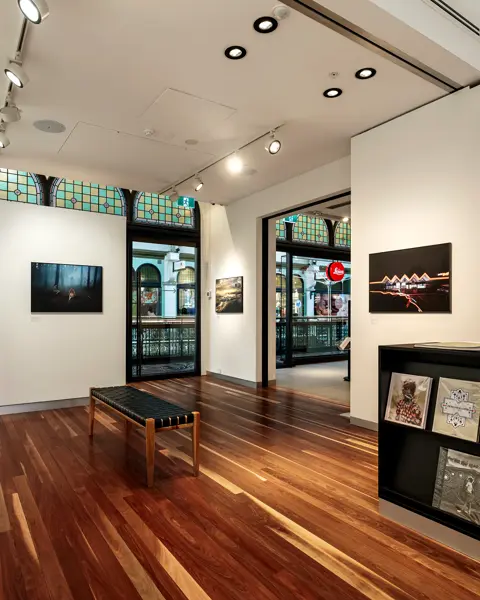 An exhibition room with a wooden floor, framed photographs, books with photo collections and a coffee machine on a counter.