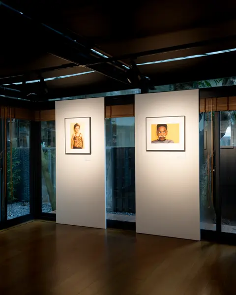 Gallery with four framed portraits of children, exhibited in a modern room with large windows.