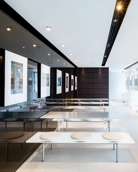 Modern exhibition room with benches and tables, framed photos and glass walls.