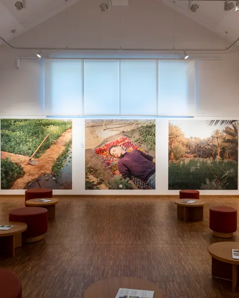 Gallery in a modern, bright design with large landscape photographs and round stools.
