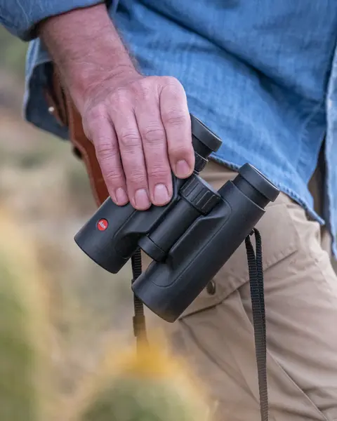 The Leica Trinovid is held in one hand by a man. He carries it casually beside him as he wanders through the landscape