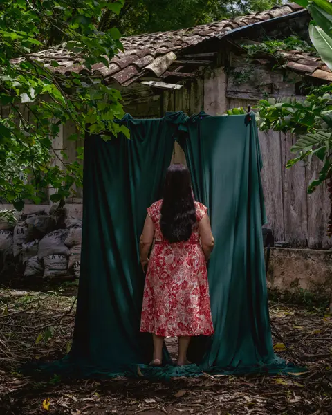 Woman in the forest walks through a green curtain behind a forest house