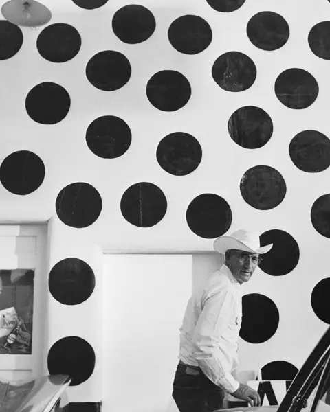 Man with hat in front of a white wall with large black dots