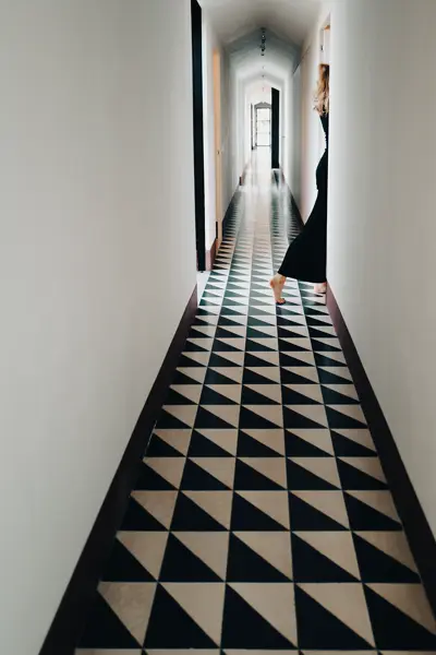 long corridor with black and white floor where a woman in a black dress walks through a door