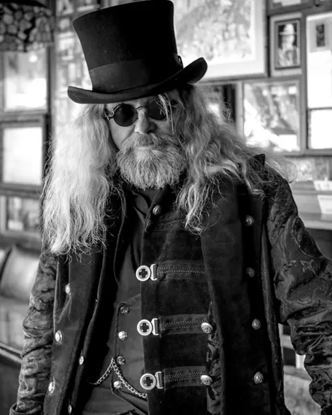Old rocker with long hair, sunglasses and top hat in a pub, black and white picture