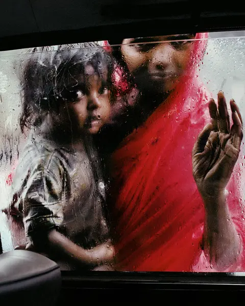 Poor woman with a child in her arms looking into a car from the outside
