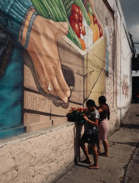 Two women with fruit baskets in front of a big fruit graffiti