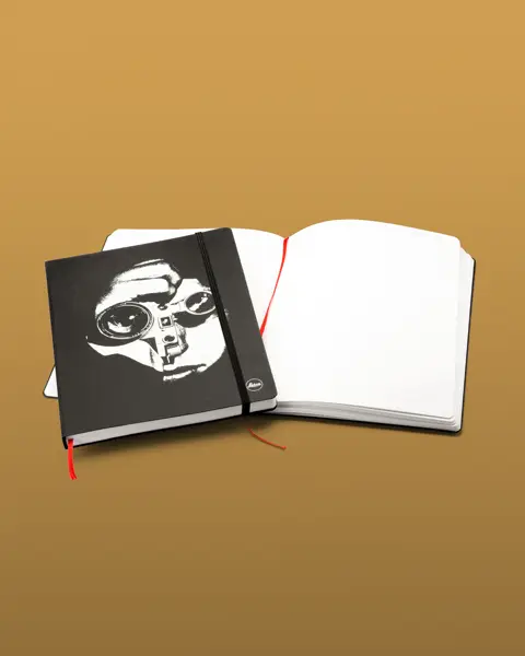 One closed notebook with black cover lying on an open notebook.