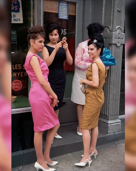 Four women standing in front of a shop with big windows.