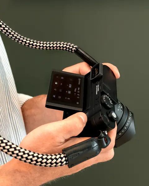 Man holding a leica Q3 Monochrom in front of a green background
