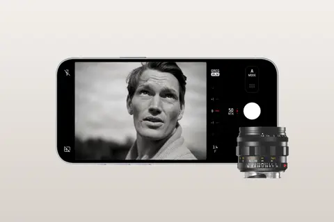 An iPhone displays an image with a man. In front of the phone is a Leica lense.