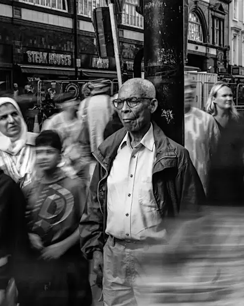 Man is leaning on a street light. Around him walking a lot of people