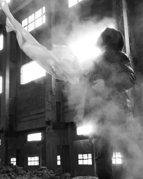 Black-and-white photograph of a man holding a white cloth in an empty old building