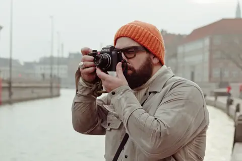 Man with orange beanie taking a photo with a Leica SL3 outdoors.