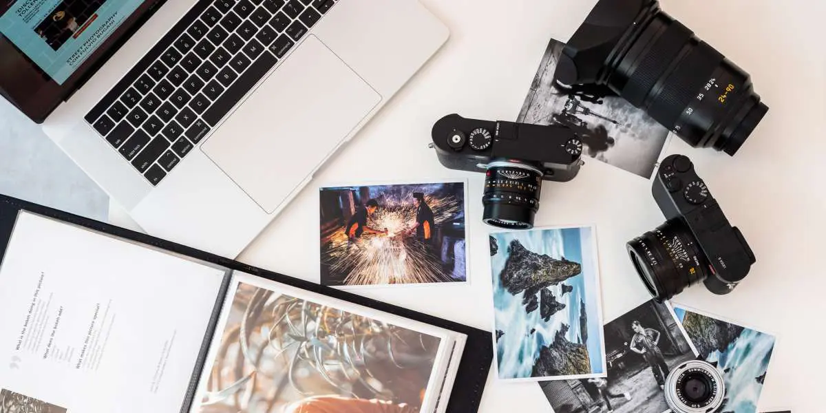 Flat lay of cameras, lenses, prints, and a photography portfolio beside a laptop.