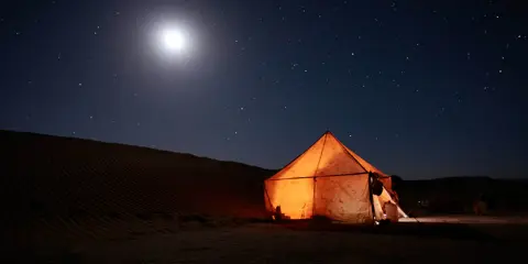 Illuminated desert tent beneath a moonlit, star-filled sky.