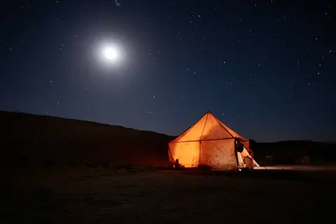 Illuminated desert tent beneath a moonlit, star-filled sky.