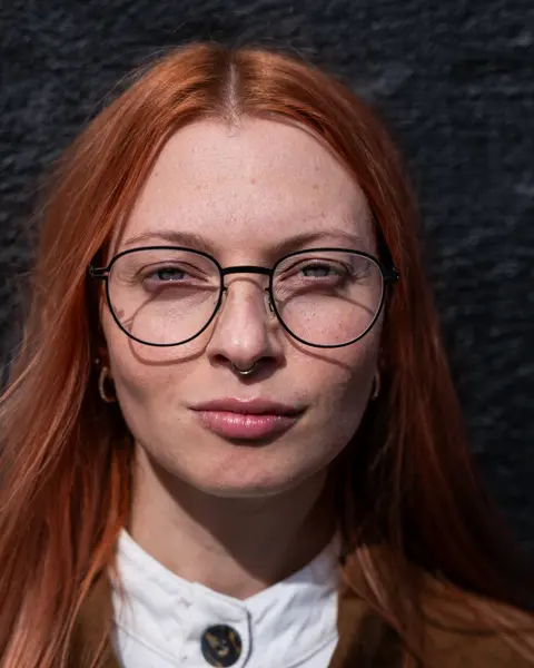 A younger woman with red long hair wears Leica Eyecare glasses.