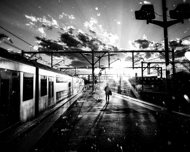 A person stands on a platform next to a train while the sun casts shadows.
