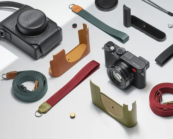 Leica camera with various straps, protective covers and accessories on a light background.