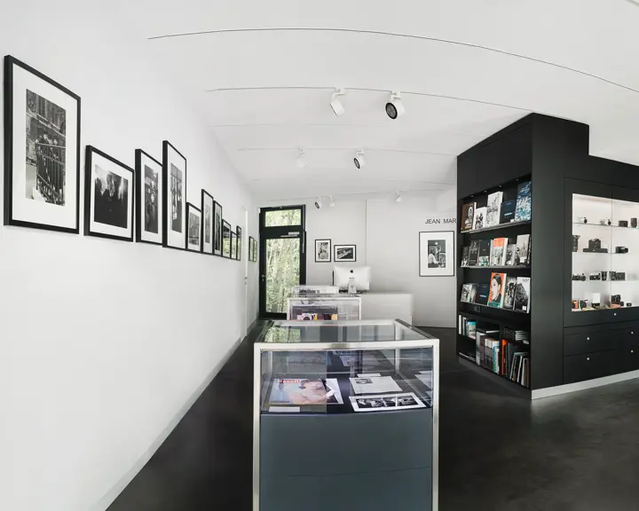 Bright exhibition room with black and white photographs, bookshelves and glass cabinets displaying cameras.