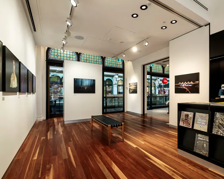 An exhibition room with a wooden floor, framed photographs, books with photo collections and a coffee machine on a counter.
