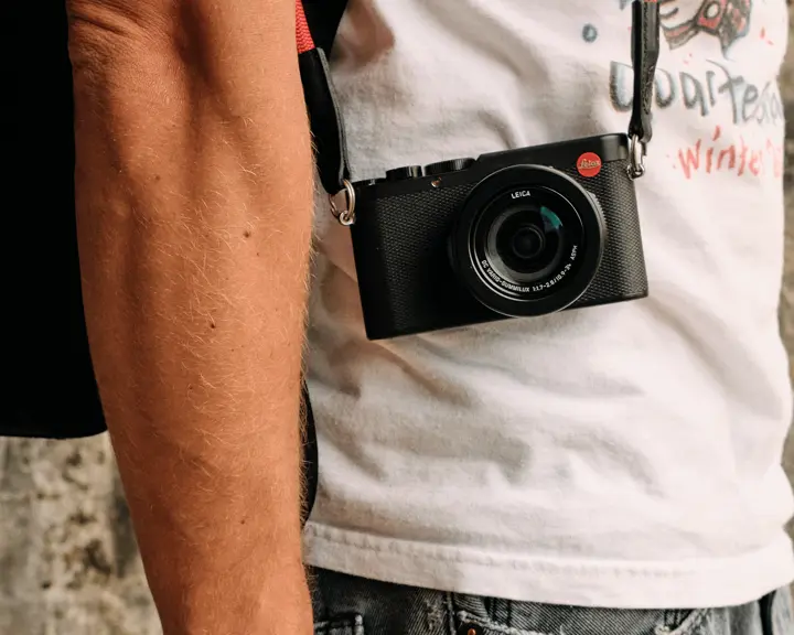 Side shot of a person with a Leica camera hanging in front of his body..