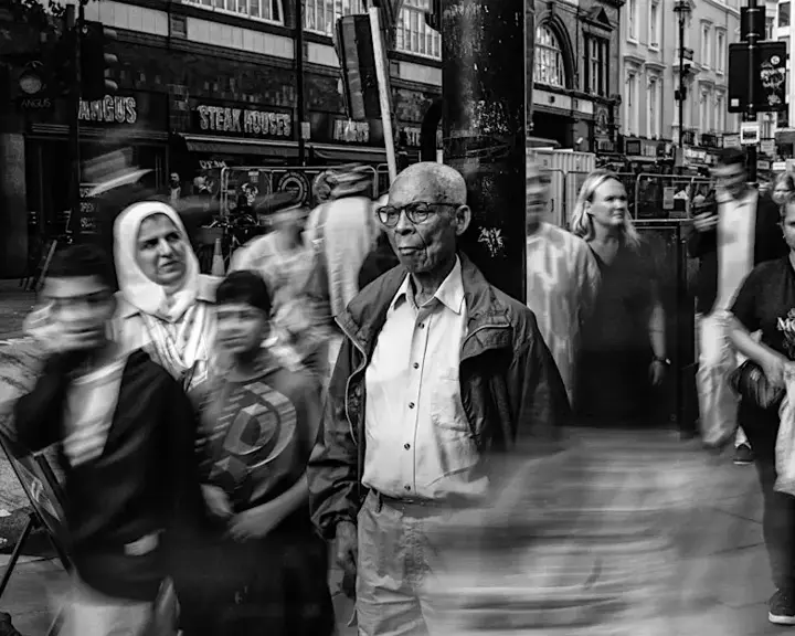 Man is leaning on a street light. Around him walking a lot of people