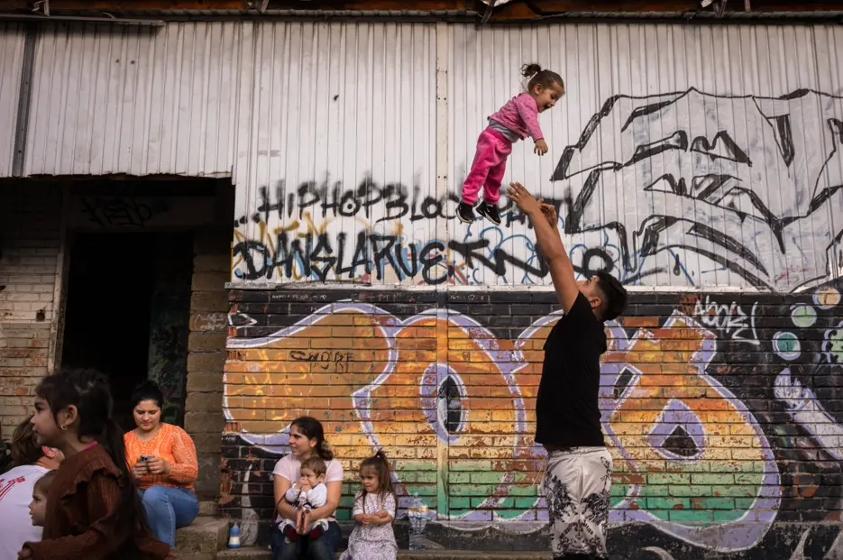 Child playing with family members in front of a graffiti-covered building, capturing everyday life, community, and urban culture.